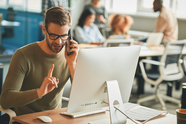 Copy space photo of calm brunette man holding index finger up while having a phonecall at his office desk