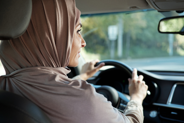 Horizontal rear view portrait shot of modern Muslim woman wearing hijab driving car looking into side-view mirror